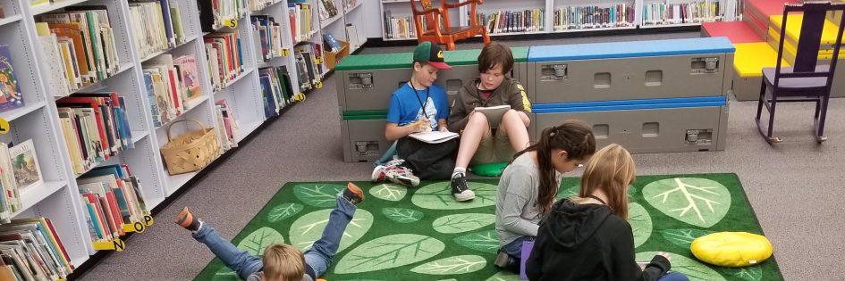 A group of five students sit on the floor reading in a school library